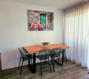 A dining area with a wooden table, black chairs, and a painting of a red scooter on the wall.