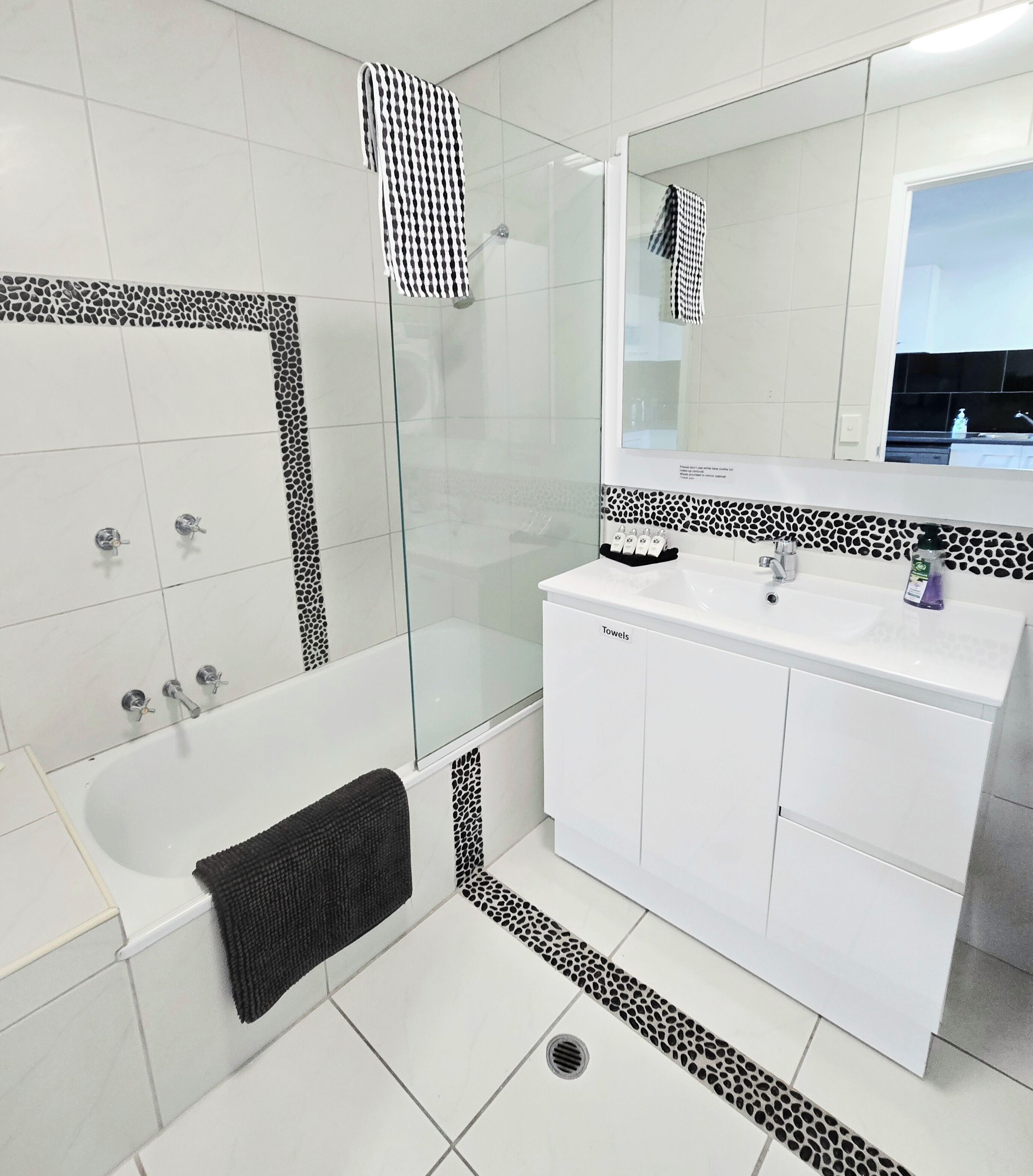 A modern bathroom with a glass-enclosed shower, white tiled walls, and a large mirror above the sink.
