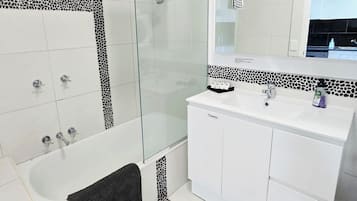A modern bathroom with a glass-enclosed shower, white tiled walls, and a large mirror above the sink.