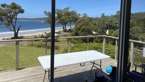 A balcony with a white table and chairs, overlooking a beach with trees and a clear blue sky. - summer beach house  (Southport)