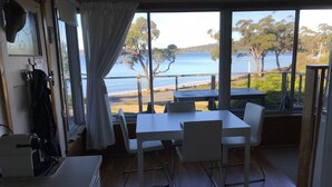 A room with a table and chairs facing a large window overlooking a beach. - summer beach house  (Southport)