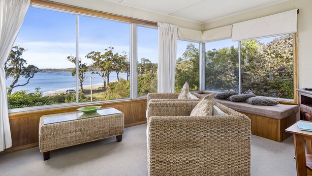 A room with large windows offering a view of the sea, wicker furniture, and a glass-top coffee table. - summer beach house  (Southport)