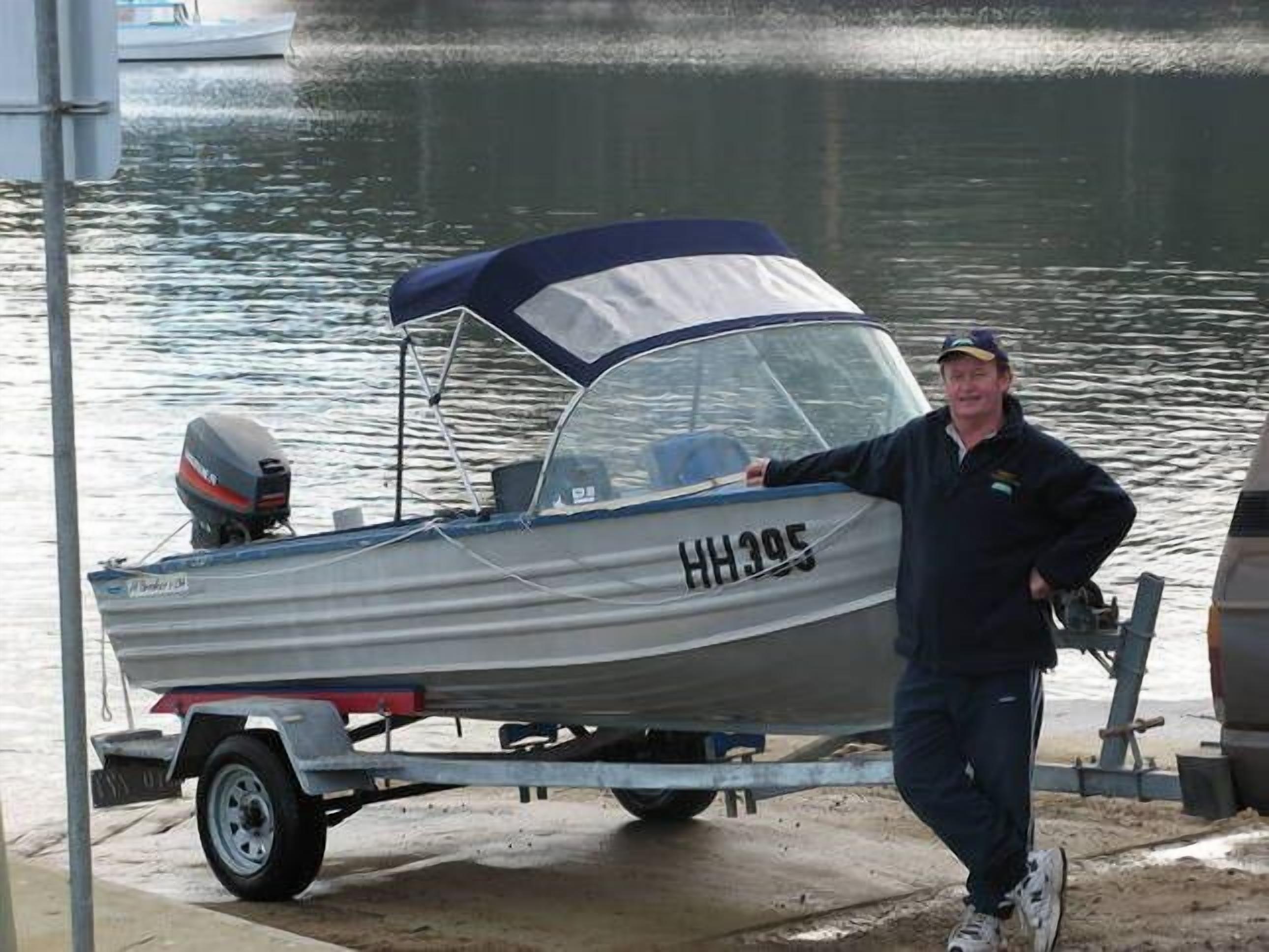 Een man staat naast een boot op een aanhanger bij een water.