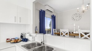 A modern kitchen with a double sink, white cabinets, a window with blue curtains, a chandelier, and a clock on the wall. - 🏖️ Absolute Beachfront Long Beach -The Beach Is Your Backyard Pet Friendly (Long Beach)