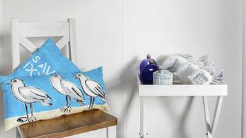 Een witte stoel met een blauw kussen waarop meeuwen afgebeeld zijn, een klein wit bijzettafeltje met decoratieve objecten, en twee ingelijste kunstwerken aan de muur.