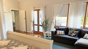 A room with a bed, a sofa, a small table, and a door leading to another room.