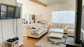 A living room with a sofa, coffee table, and a TV. There is a kitchen area in the background.