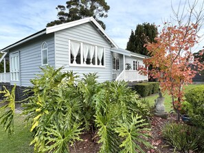 A house with a porch, a garden with various plants, and a tree with autumn leaves.