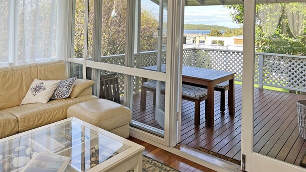A cozy living room with a sofa, a glass coffee table, and a view of a wooden deck and outdoor scenery.