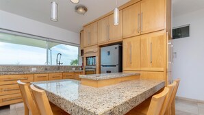 A modern kitchen with granite countertops, wooden cabinets, and a large island with bar stools. - Spectacular Master Penthouse - Best Ocean view and sunsets on the Sea of Cortez (La Paz)