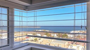 A room with a large window overlooking a coastal area, featuring a clear view of the sea and buildings. - Spectacular Master Penthouse - Best Ocean view and sunsets on the Sea of Cortez (La Paz)