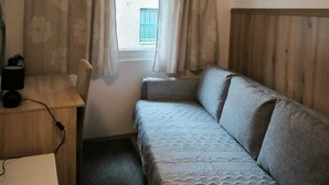 Un petit logement composé d’une seule pièce, avec une tête de lit en bois, un bureau avec une lampe et un lit recouvert d’une couette à motifs.
