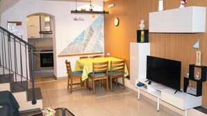 Un salon moderne comprenant un coin repas, un téléviseur et un escalier menant à la cuisine.