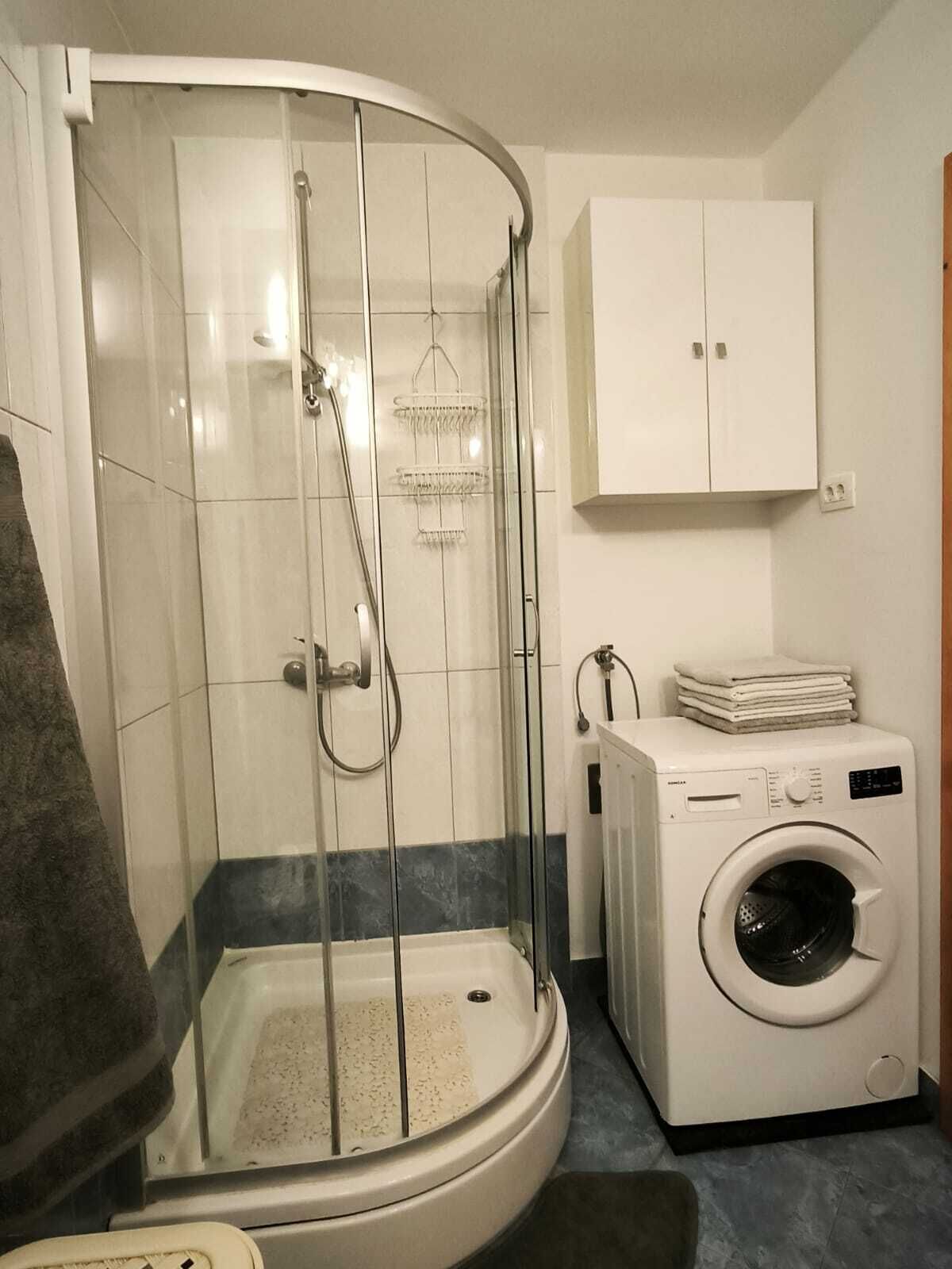 A modern bathroom with a glass-enclosed shower, a built-in washing machine, and a white cabinet.