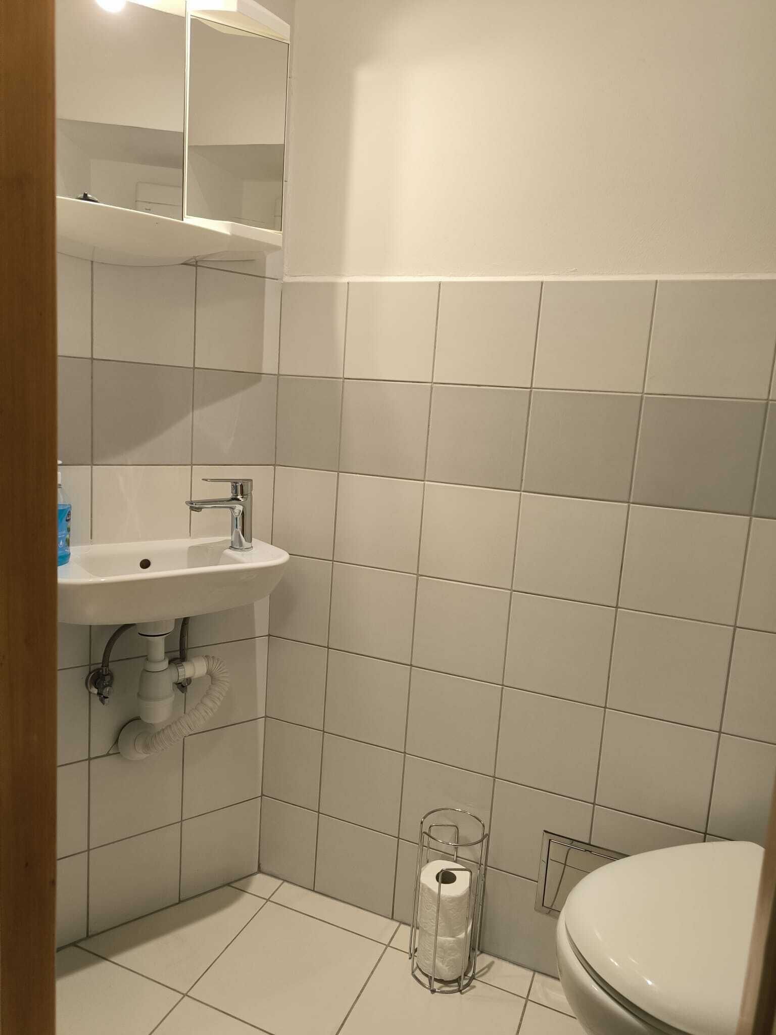 Un bagno piccolo e pulito, con piastrelle bianche, un lavandino e un water.
