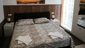 Une chambre à coucher avec une couvre-lit à motifs zébrés, une table de chevet avec une lampe, un tableau représentant un coucher de soleil et une fenêtre avec des rideaux.