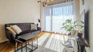 A modern living room with a grey sofa, a black coffee table, and a large window with sheer curtains. - Sunny Balcony Suite by Rotermann City Apts (Tallinn)