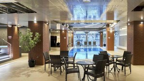 A modern indoor pool area with a central pool, surrounded by wicker chairs and tables, and brick pillars. - Sunny Balcony Suite by Rotermann City Apts (Tallinn)