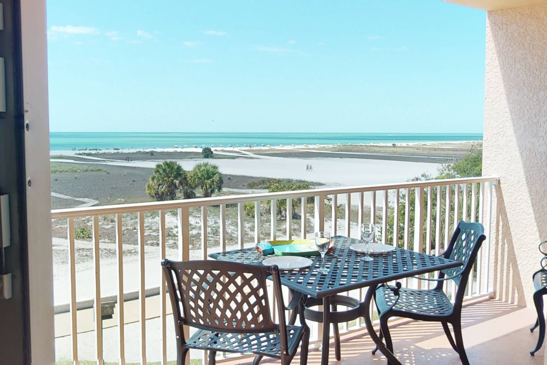 A balcony with a table and chairs overlooking a beach.