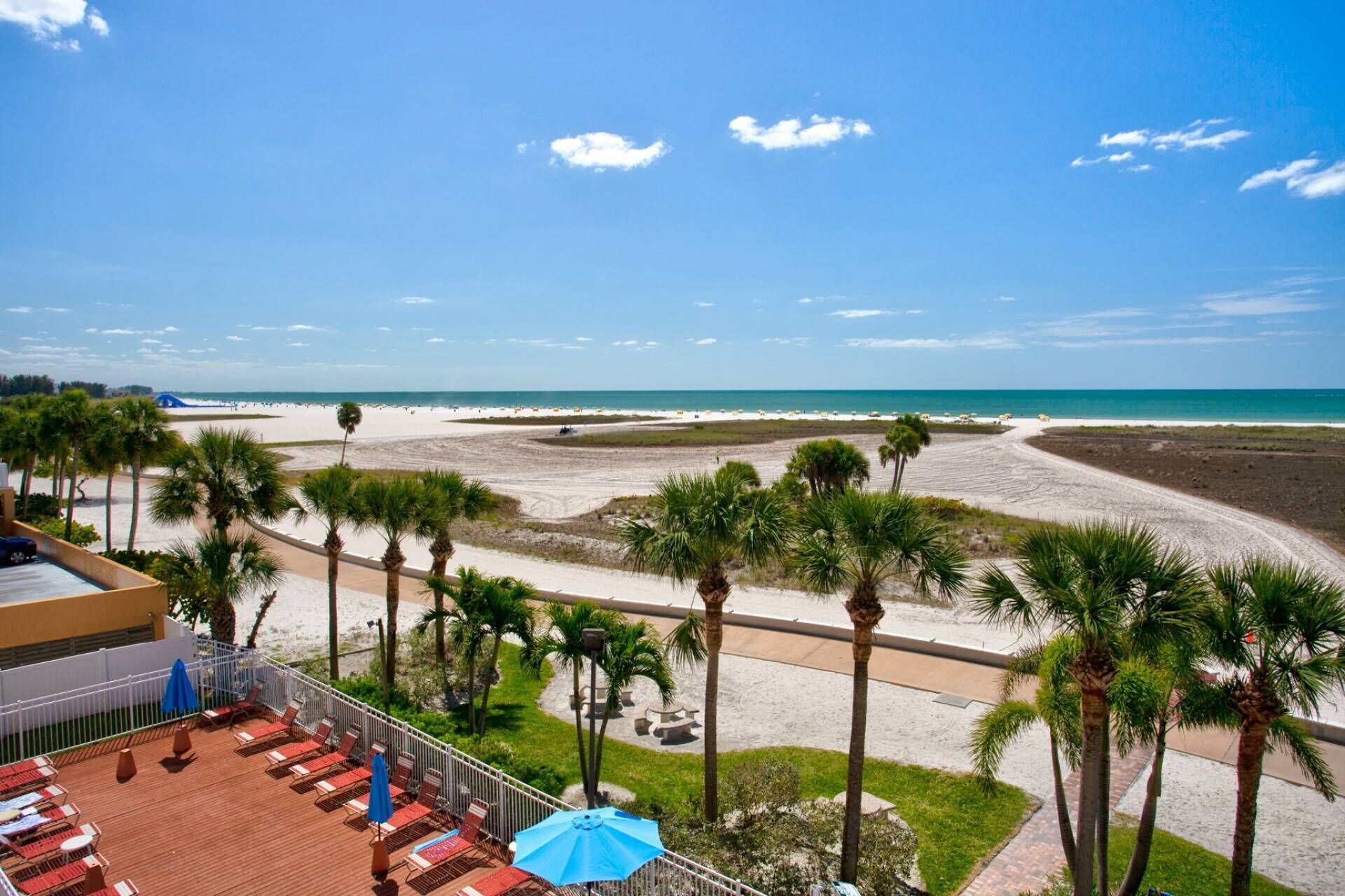 A beach view from a resort balcony with palm trees, a sandy beach, and a clear blue sky.