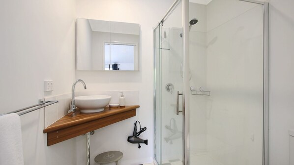 Ein modernes Badezimmer mit Duschkabine aus Glas, einem weißen Waschbecken mit Holzablage und einem Spiegel darüber.