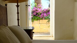 Un dormitorio con una cama, una lámpara y vistas a una palmera y flores a través de una puerta abierta.
