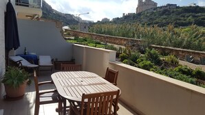 Une terrasse avec une table et des chaises, des plantes en pot et une vue sur une colline parsemée de bâtiments.