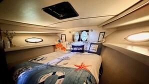 A compact bedroom with a bed, a small shelf with decorative items, and a ceiling vent.