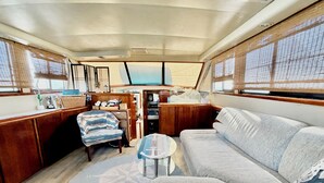 A cozy interior with a sofa, armchair, and small table, wooden cabinets, and a window with blinds.