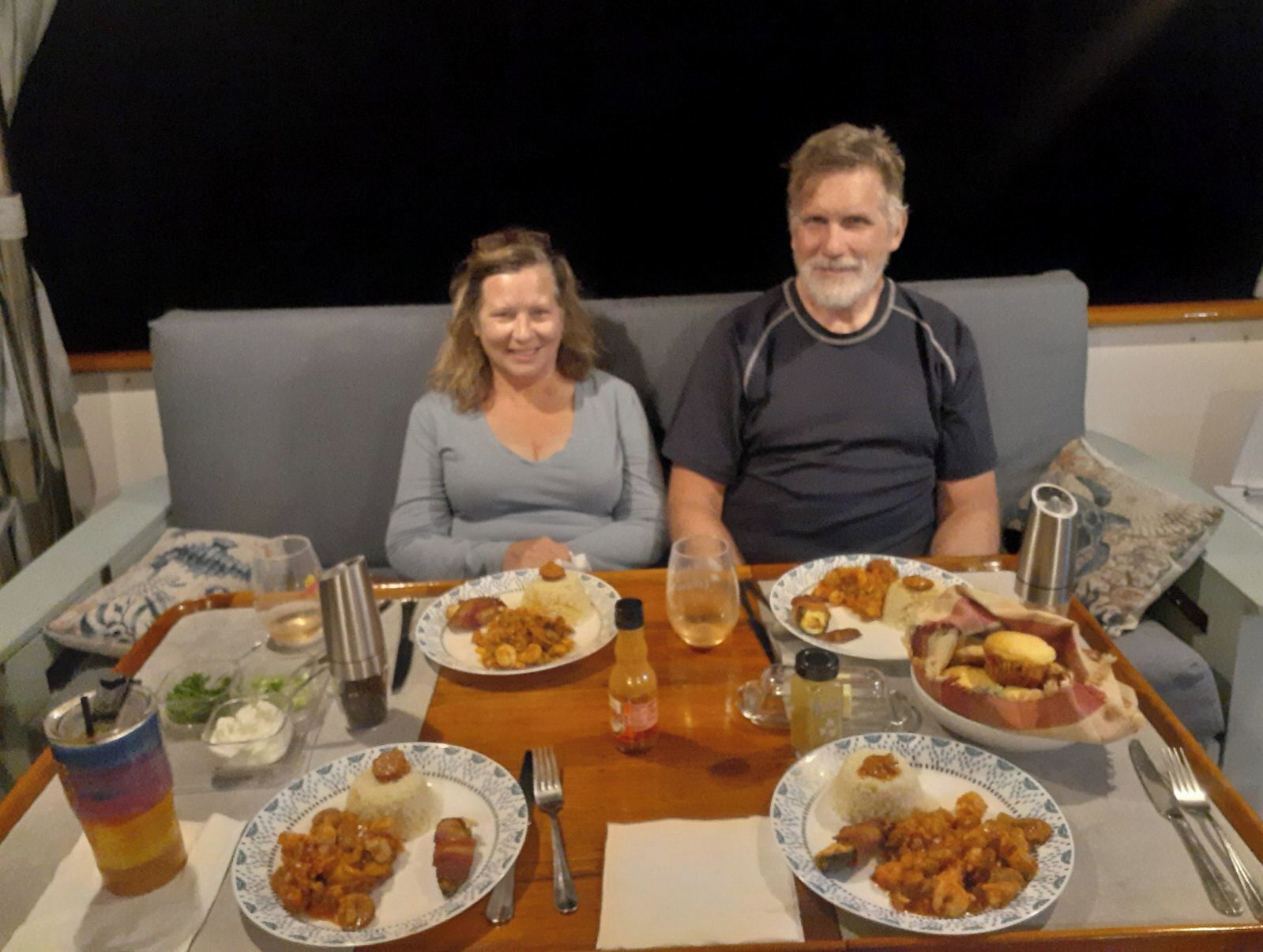 Two people dining at a table with plates of food, a drink, and condiments.