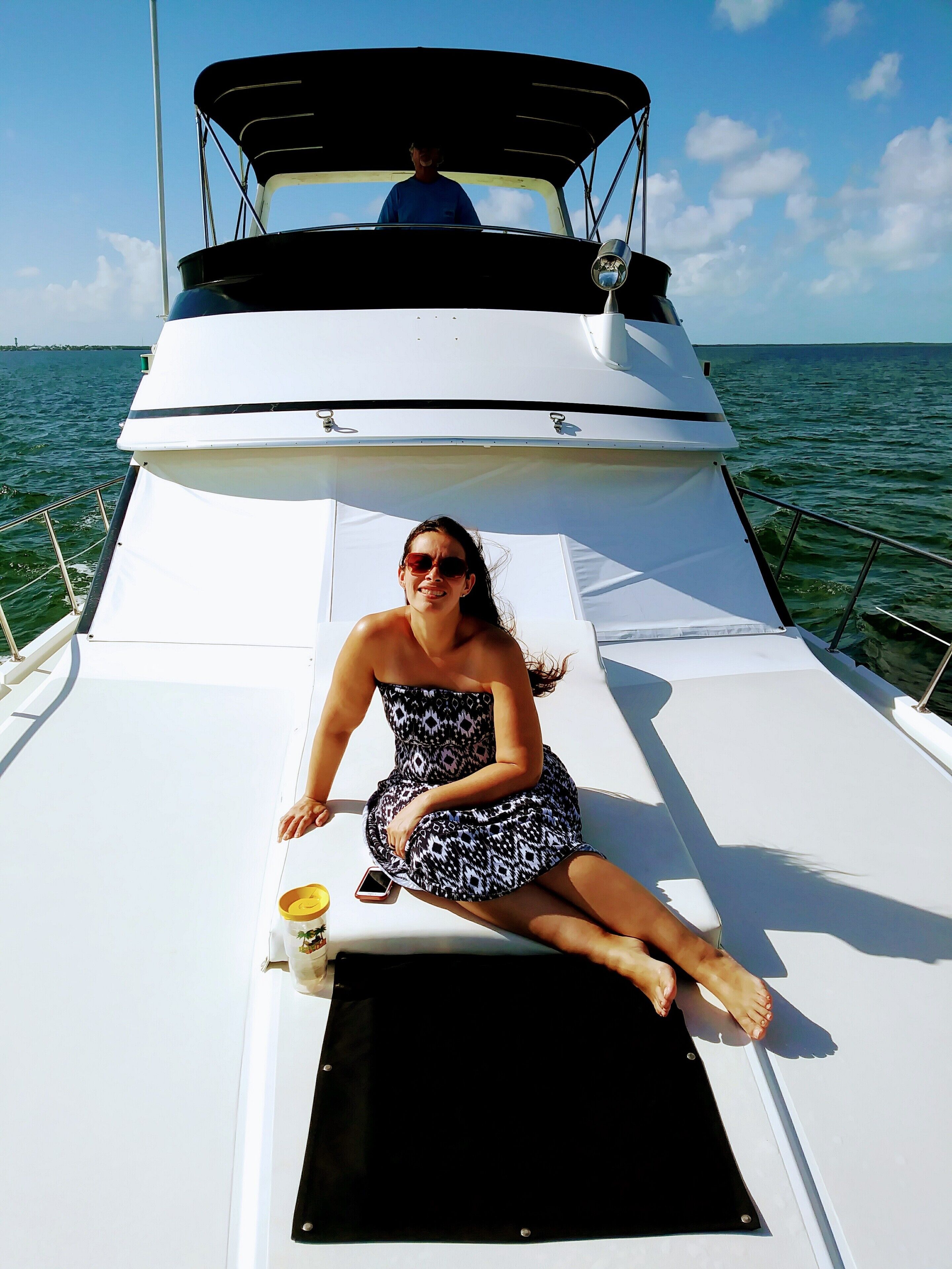 A person sitting on a boat with a cup and a smartphone on the deck.
