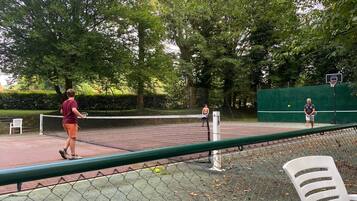 Un campo da tennis all'aperto con una rete, circondato da alberi e un canestro da basket.