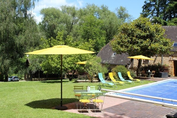 Un patio trasero con piscina, mobiliario exterior y una casa de piedra.