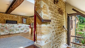 Un interior rústico de piedra con una escalera de madera, un sofá y vistas al exterior con vegetación.