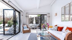 A modern living room with a glass coffee table, a white sofa with orange cushions, and a wicker chair.