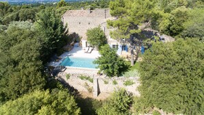 A stone villa with a swimming pool surrounded by dense greenery and a view of distant hills.