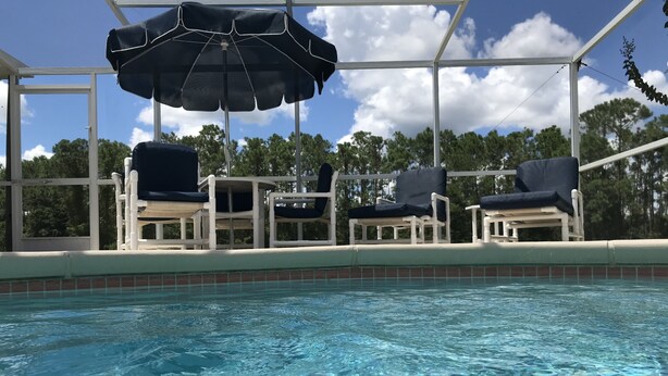 A pool area with clear water, white lounge chairs, and a covered seating area with an umbrella. - Premier Host Rated Villa - Private solar heated pool & family games room   (Davenport)
