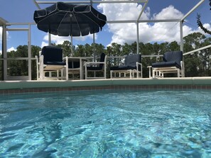 Una piscina con agua cristalina, sillas de descanso blancas y una zona de estar cubierta con una sombrilla.