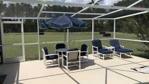 An outdoor patio with a pool, covered seating area, and a view of a grassy field. - Premier Host Rated Villa - Private solar heated pool & family games room   (Davenport)