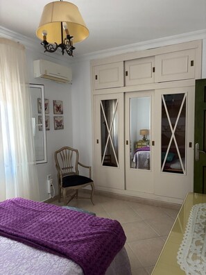 Ein Schlafzimmer mit einem Bett, einem Sessel, einem Kleiderschrank mit Spiegeln und einer Deckenleuchte.