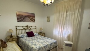A bedroom with a bed, bedside tables, a lamp, a heater, and a painting on the wall.