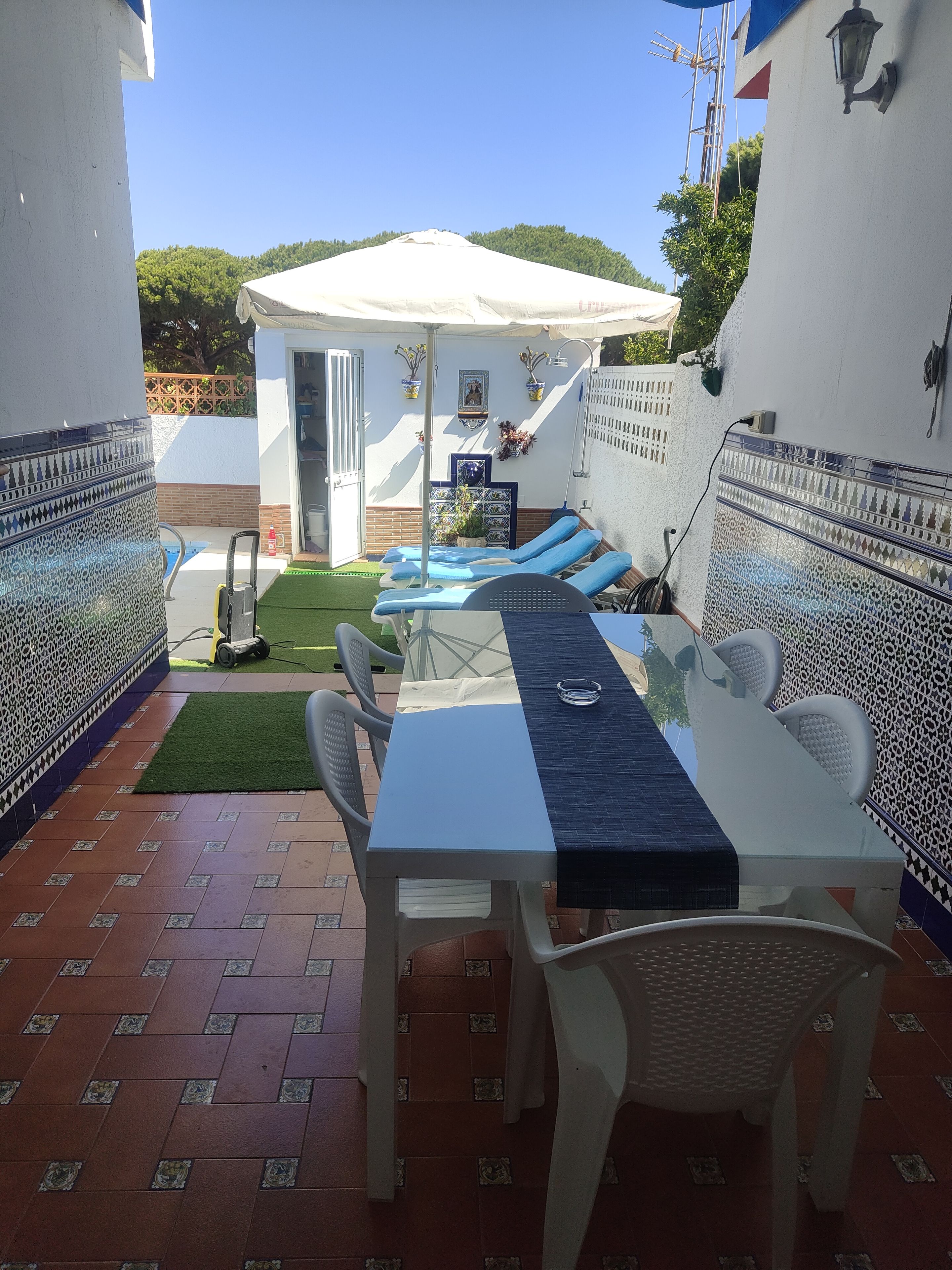 Un patio con mesa y sillas, una zona de estar cubierta y un pequeño jardín.