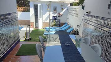 Un patio con mesa y sillas, una zona de estar cubierta y un pequeño jardín.