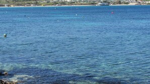 A coastal view with clear blue water, a distant shoreline with buildings, and a hill with greenery. - The Moll Apartment - Seaside Holiday Home (Il-Mellieha)
