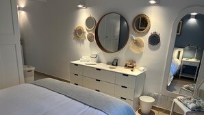 A bedroom with a bed, a dresser, a vanity with a mirror, and a small table with a chair. - The Moll Apartment - Seaside Holiday Home (Il-Mellieha)