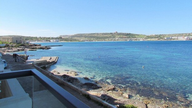 A coastal view with clear blue water, rocky shoreline, and distant hills. - The Moll Apartment - Seaside Holiday Home (Il-Mellieha)