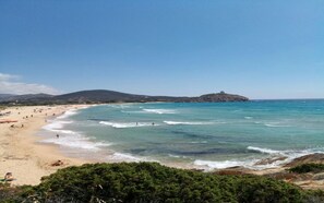 A beach with clear turquoise waters, sandy shore, and a hill with a structure on top. - Villa Pepa S'abuleu, detached villa with garden and swimming pool. (Pula)