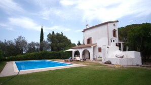 Eine weiße Villa mit Swimmingpool, Garten und einem hohen Baum.