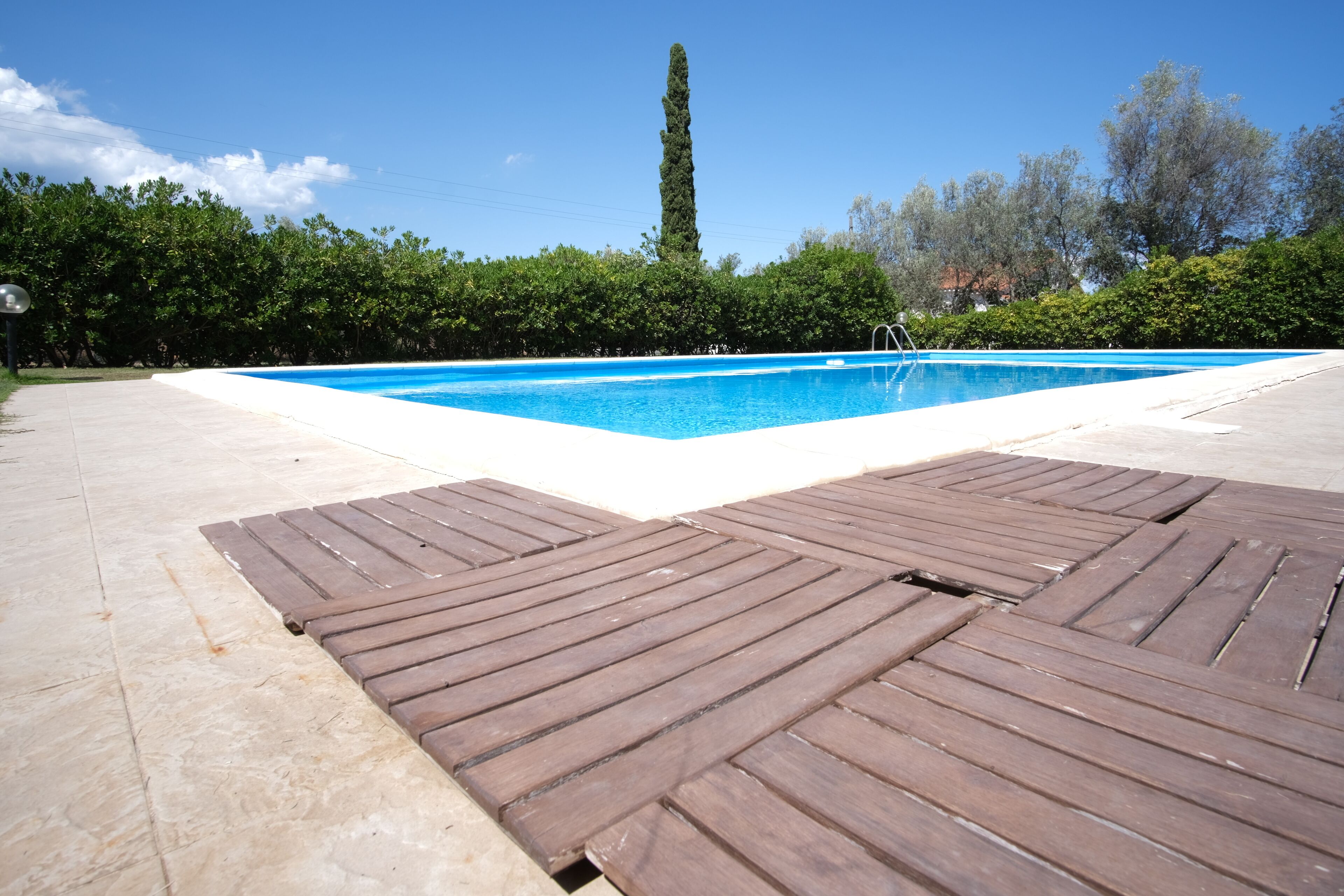 A swimming pool with a wooden deck in the foreground and a tall tree in the background.