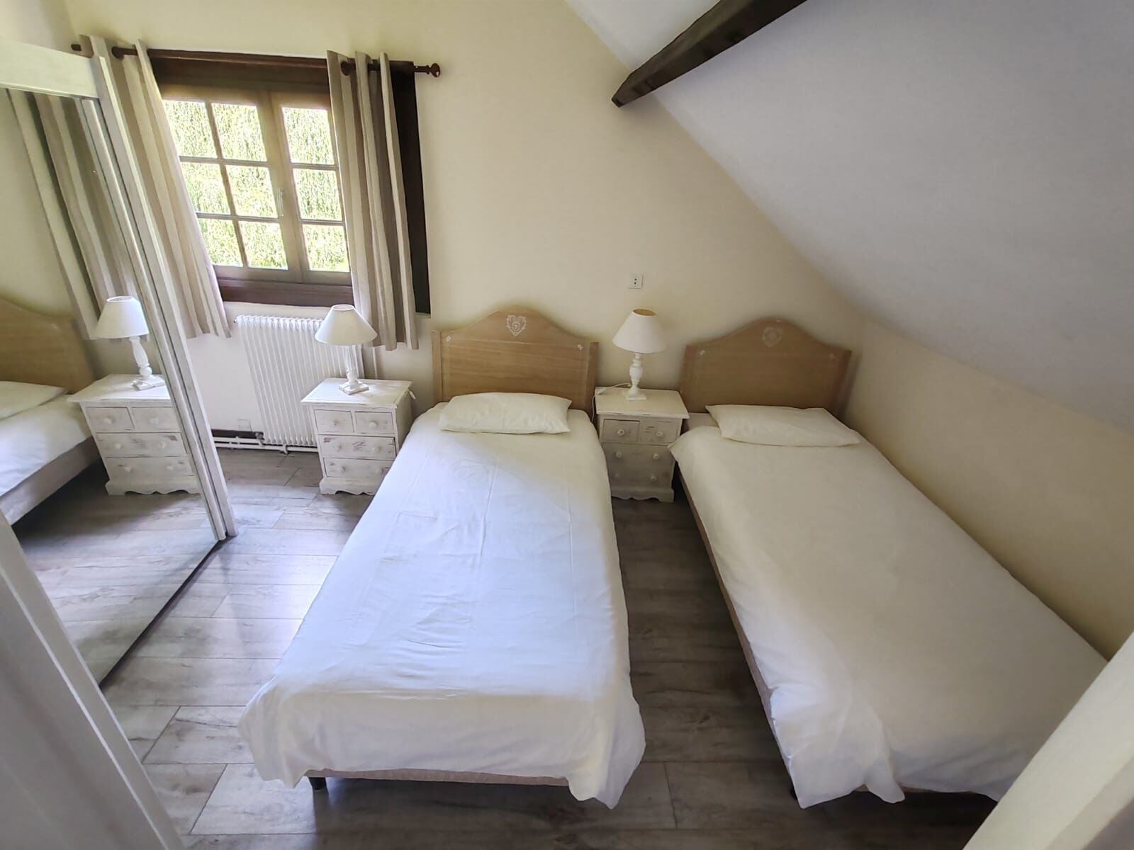 Un dormitorio con dos camas individuales, una ventana con cortinas, un radiador y un techo de madera.
